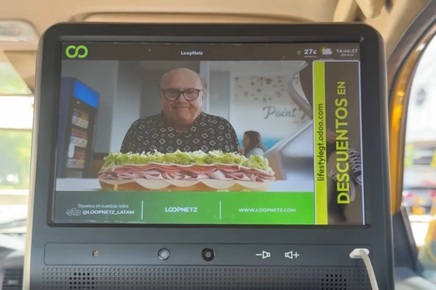 Pantalla LED en el respaldo del asiento delantero de un vehículo, vista desde atrás. Muestra el anuncio de una marca de comida con un descuento en la franja lateral.